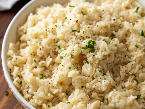 Cooked white rice pilaf in textured white bowl with chopped parsley on top.