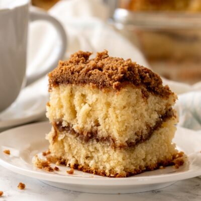 Slice of baked coffee cake on white plate near white mug.