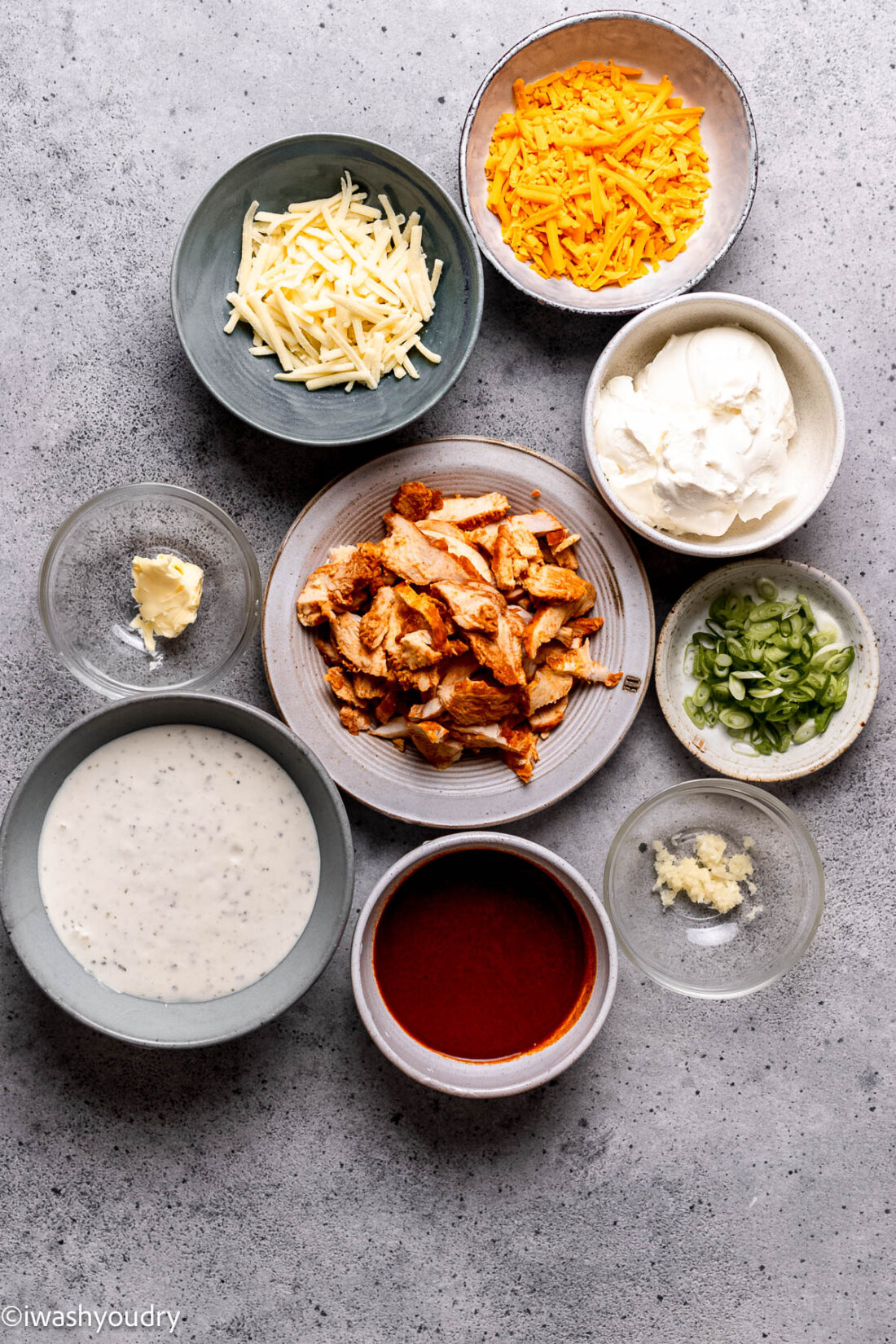 Ingredients for buffalo chicken dip in glass dishes on marble countertop. 