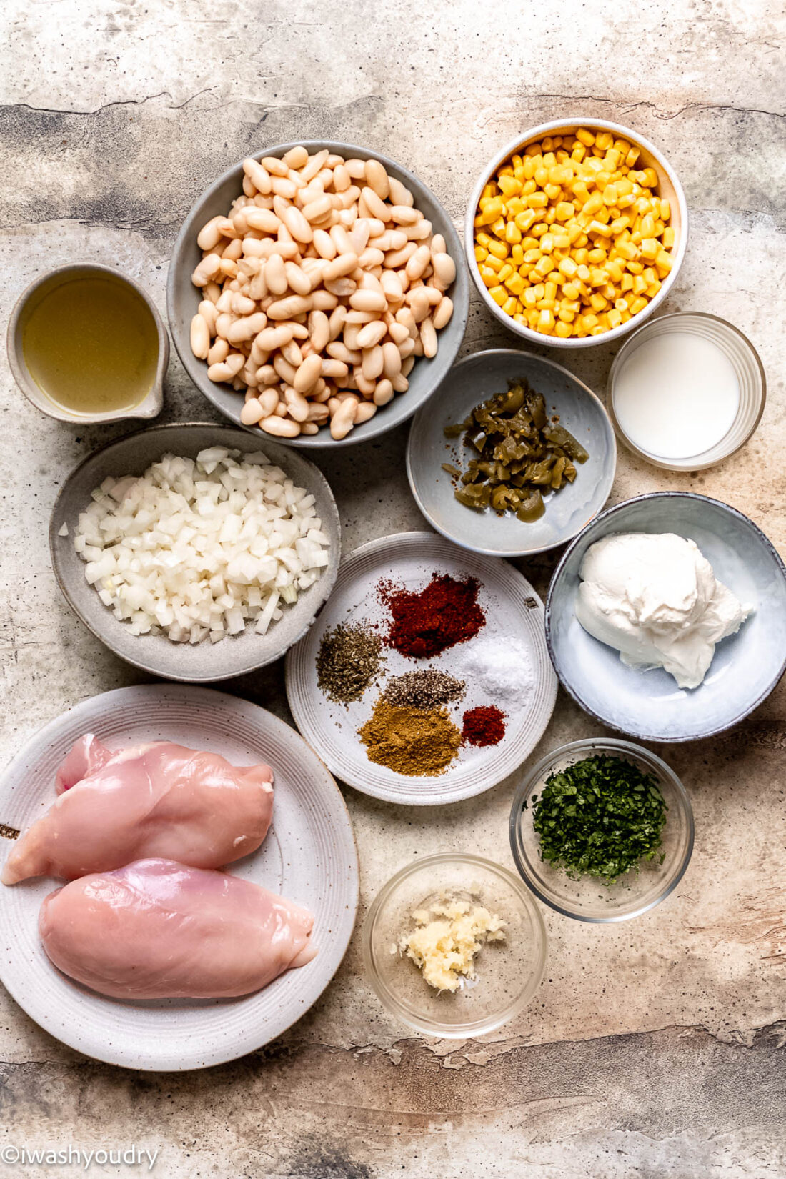 Ingredients for white chicken chili in ceramic bowls on marble countertop. 