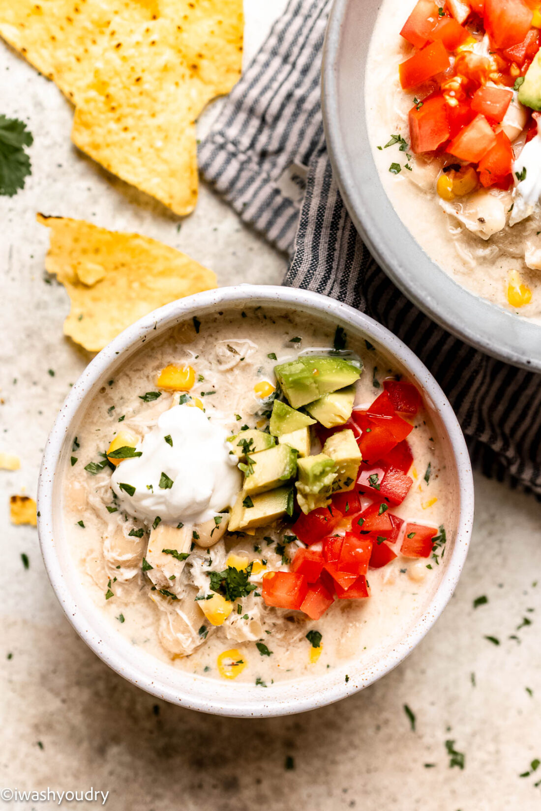 Cooked white chicken chili in white bowl with avocado and tomato. 