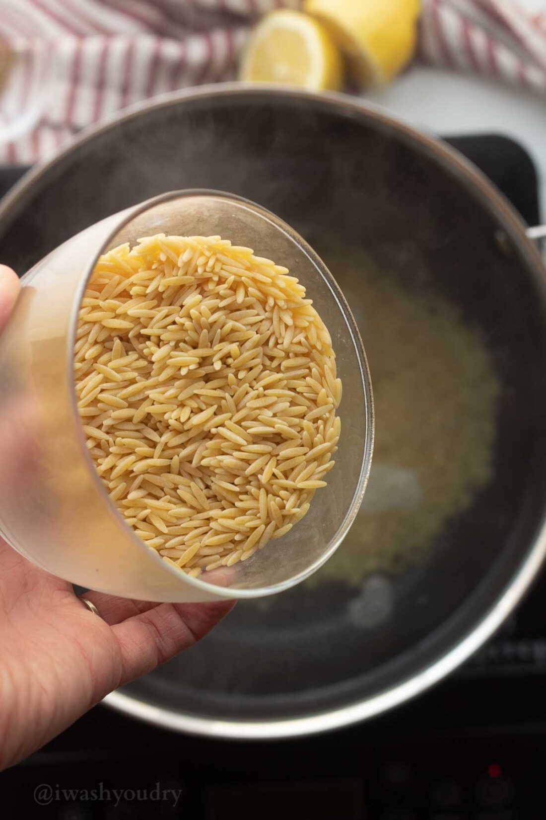 Uncooked orzo pasta in glass bowl above pot of oiling water. 