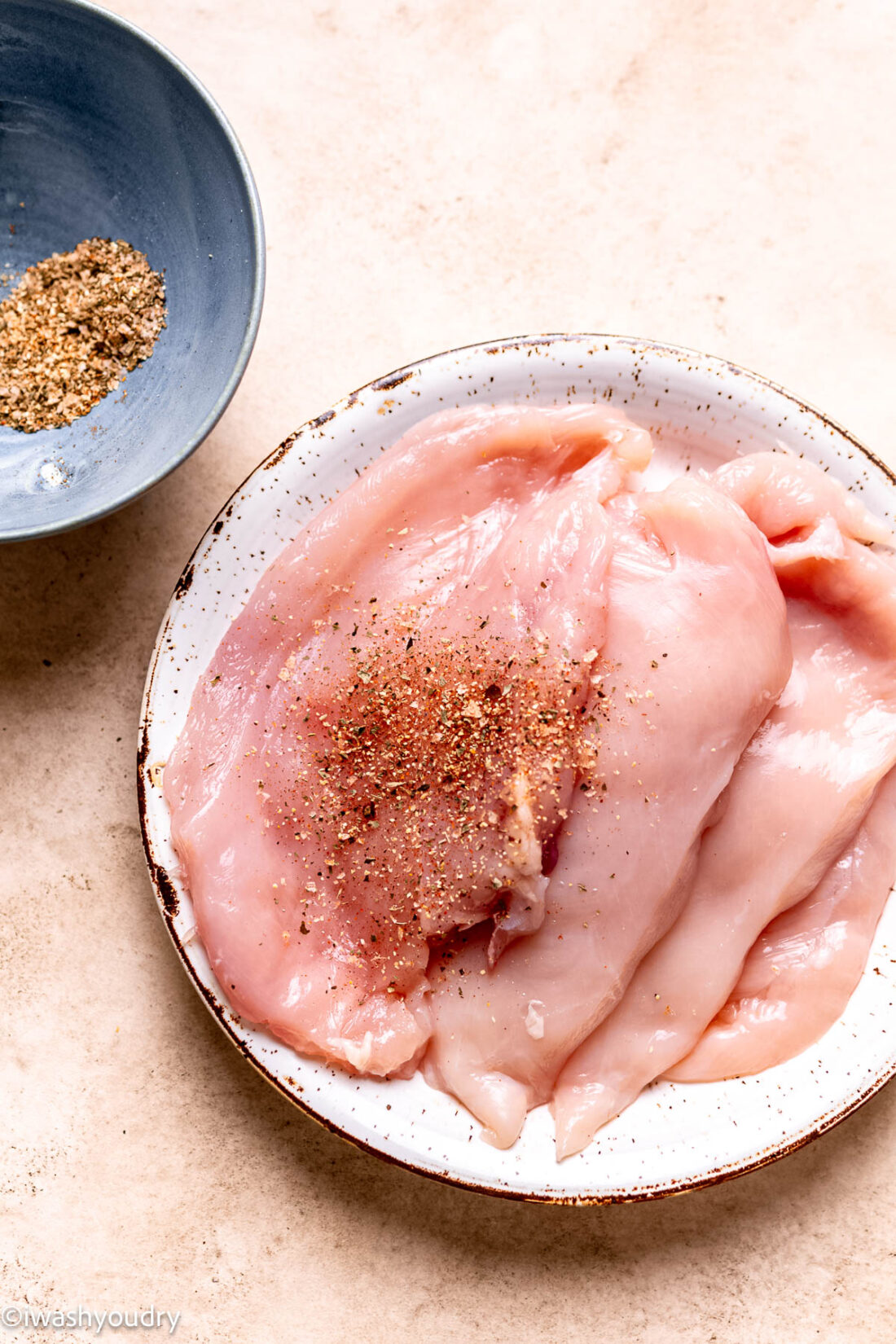 Raw chicken with seasoning on ceramic plate. 