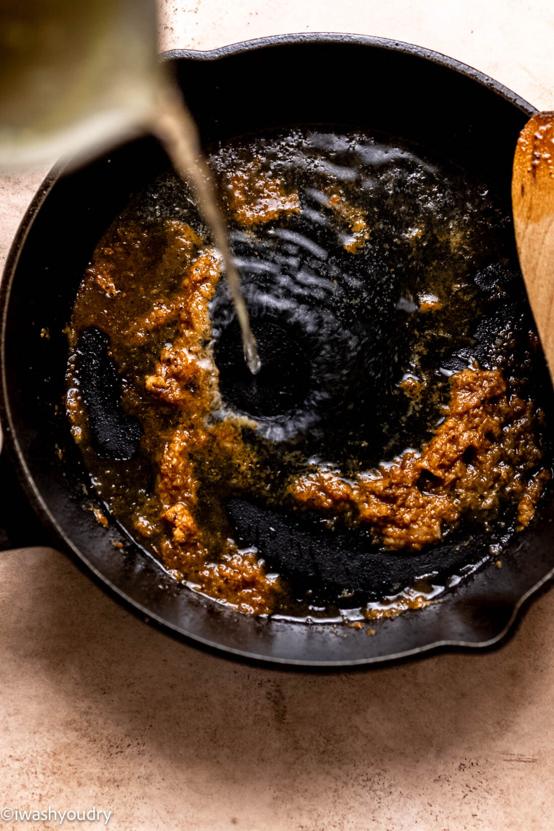 Pouring chicken broth into metal frying pan with garlic. 