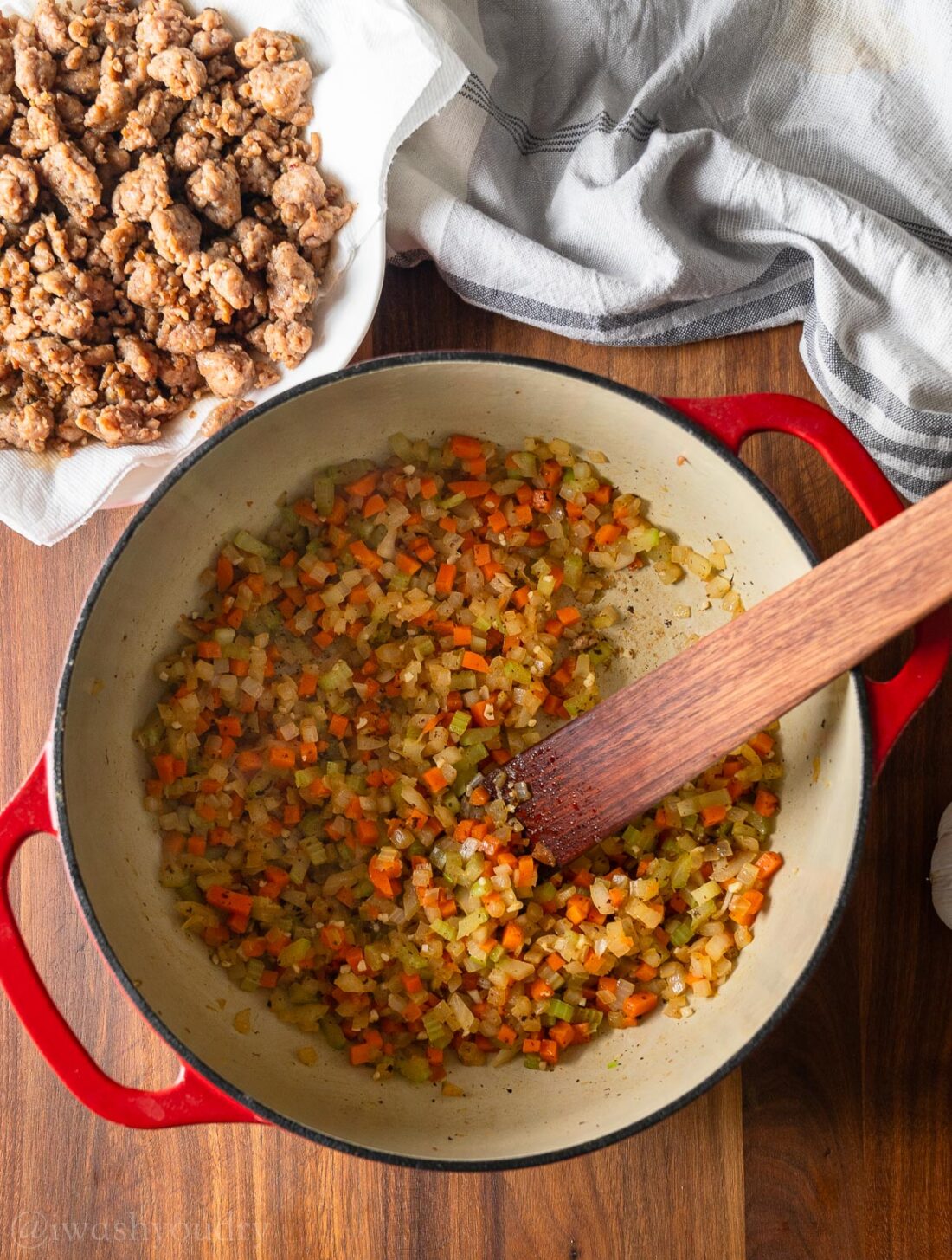 sautéing the veggies in a stock pot with cooked sausage on a plate nearby.