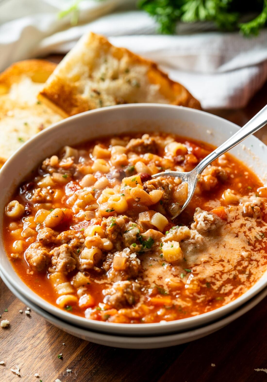 spoonful of pasta fagioli in white bowl with a side of crusty bread.