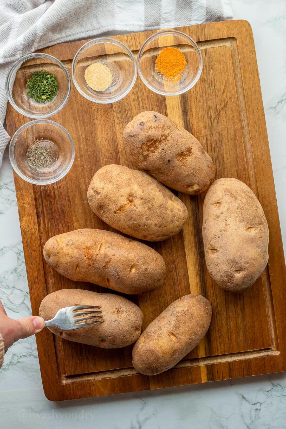 Piercing potato with fork on wooden surface.