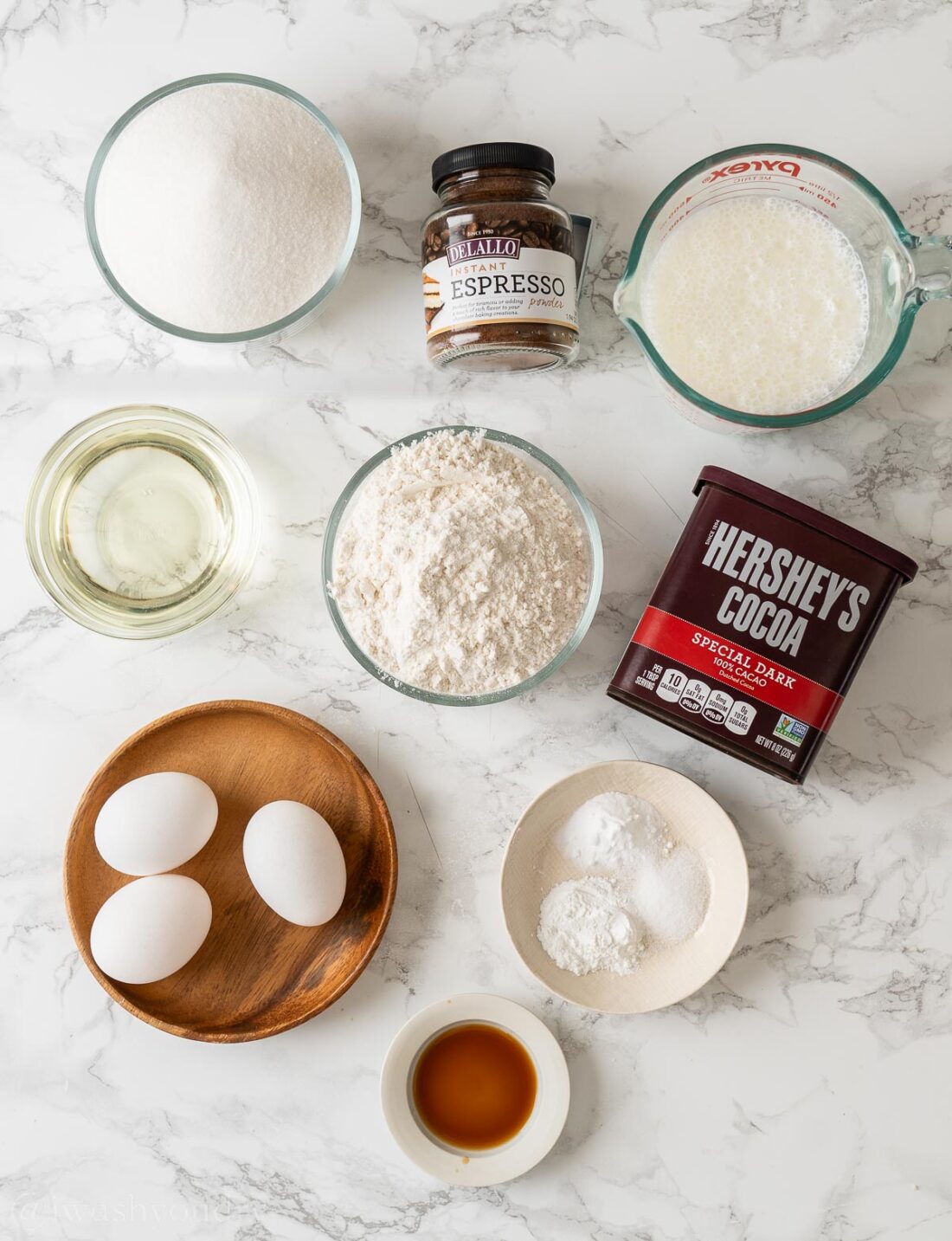 ingredients for chocolate cake on white surface with cocoa powder and espresso powder.