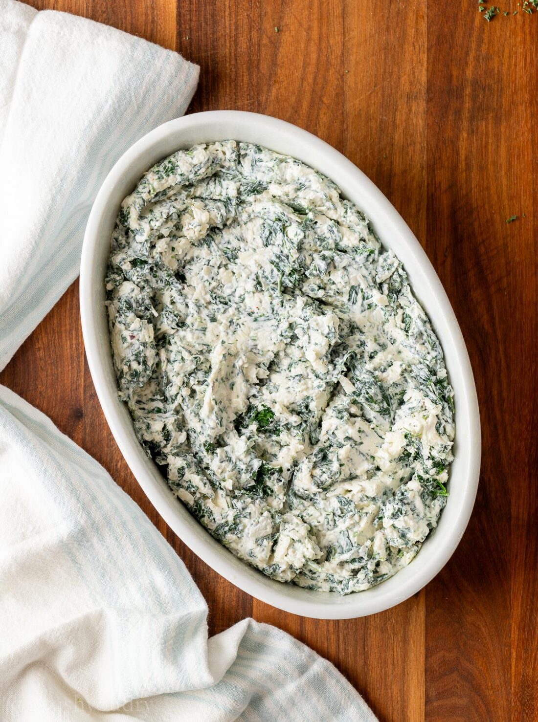 spinach dip in white casserole dish on wooden surface.