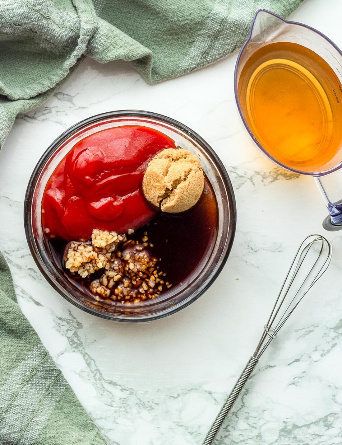 Sweet and sour sauce ingredients in a glass bowl next to a wire whisk. 