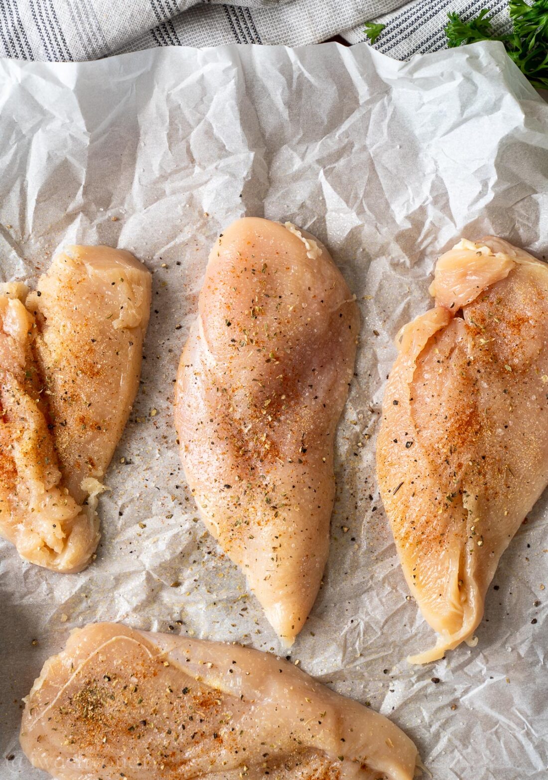 Raw seasoned chicken on parchment paper,.