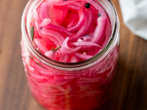 Pickled red onions in glass jar on wood cutting board.