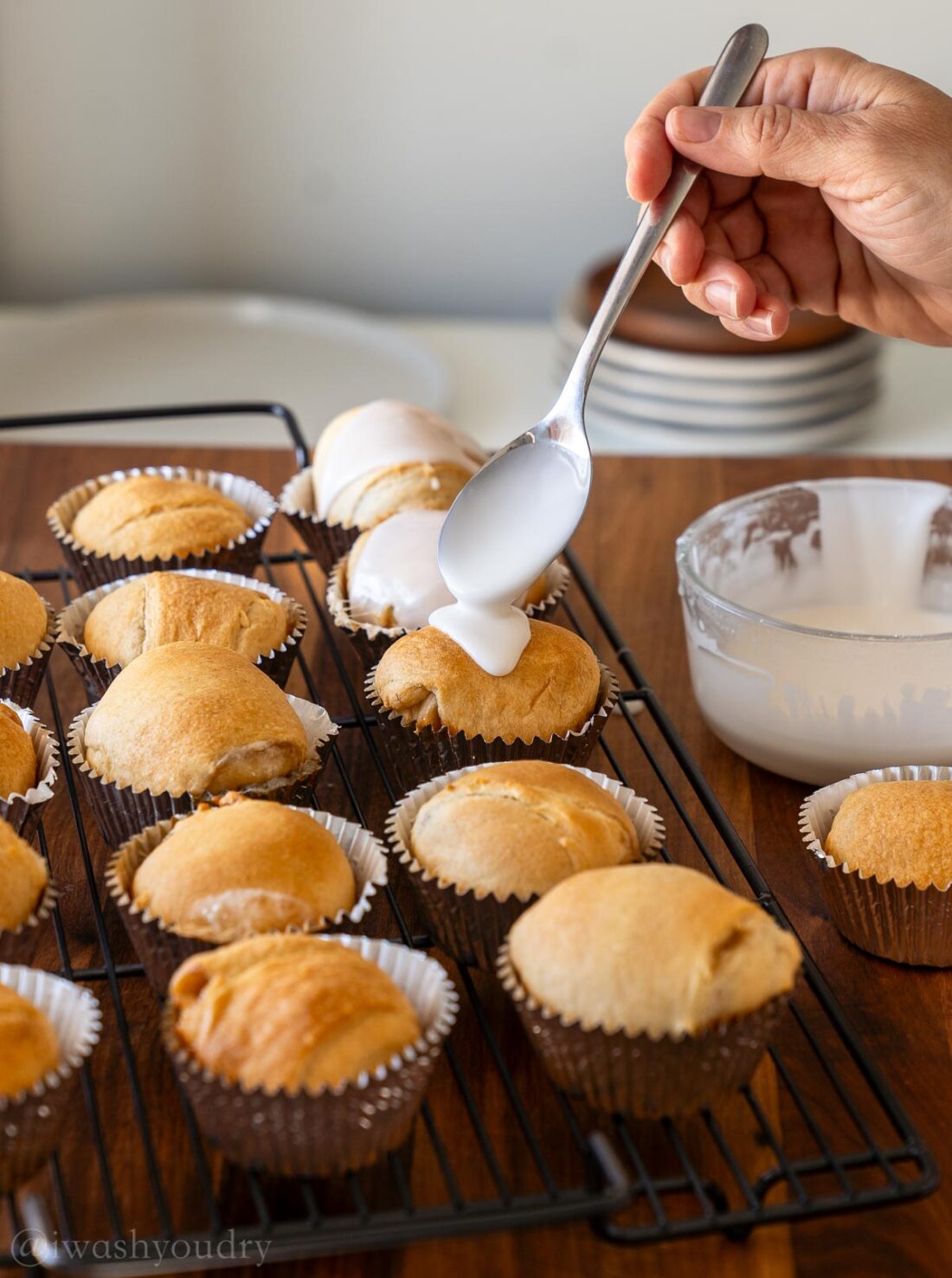 spooning sugar icing over rolls on wire rack.