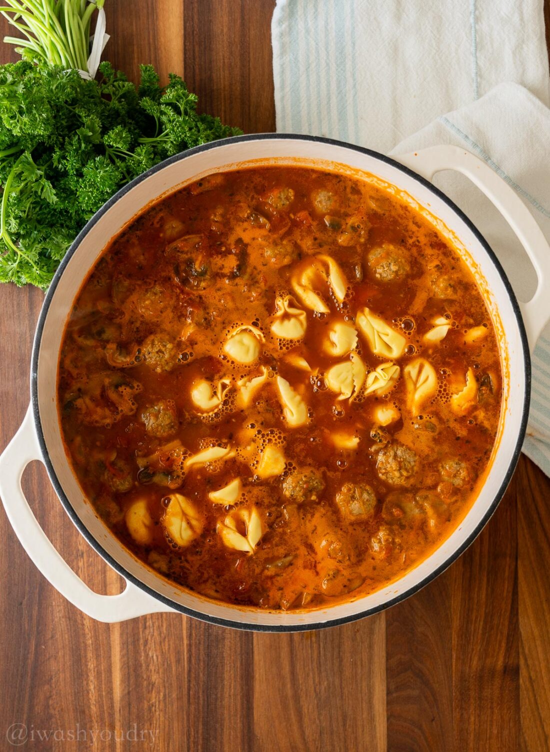 Tortellini and meatballs added to soup in white pot. 