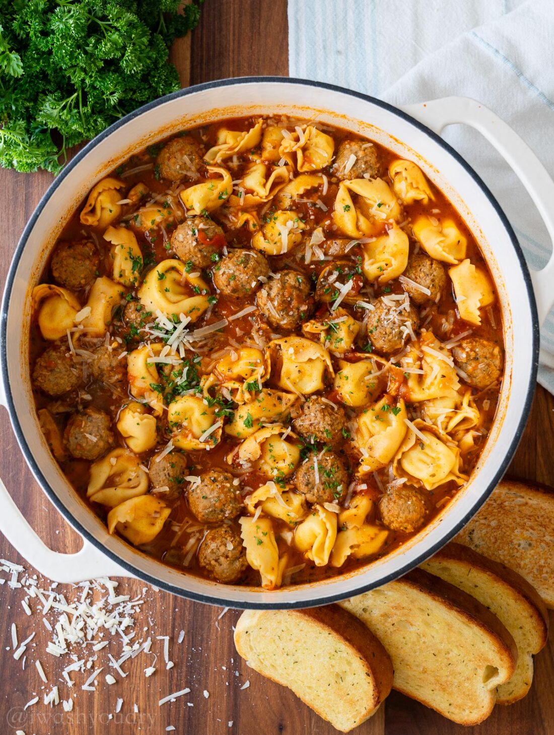 Cooked meatball tortellini soup in white pot with parsley and parmesan on top. 