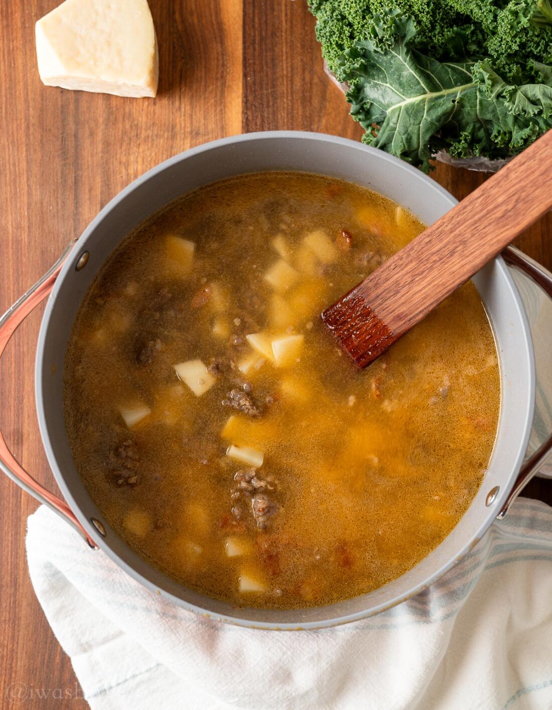 Boiled potatoes, sausage, bacon, and chicken broth in pot with wod spatula. 