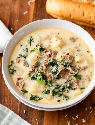 Bowl of zuppa toscana soup in white bowl on wood cutting board with breadstick.