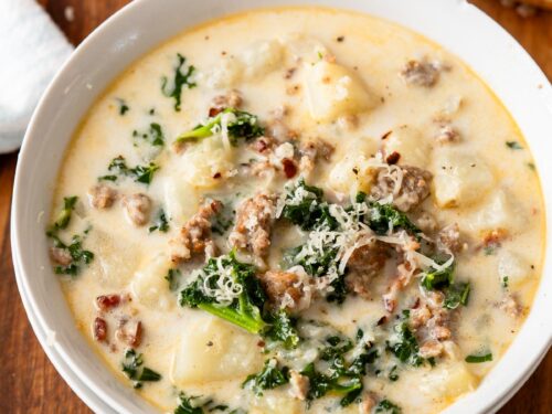 Bowl of zuppa toscana soup in white bowl on wood cutting board with breadstick.