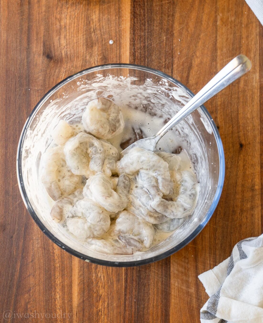 shrimp coated in a white cornstarch slurry with fork in bowl.