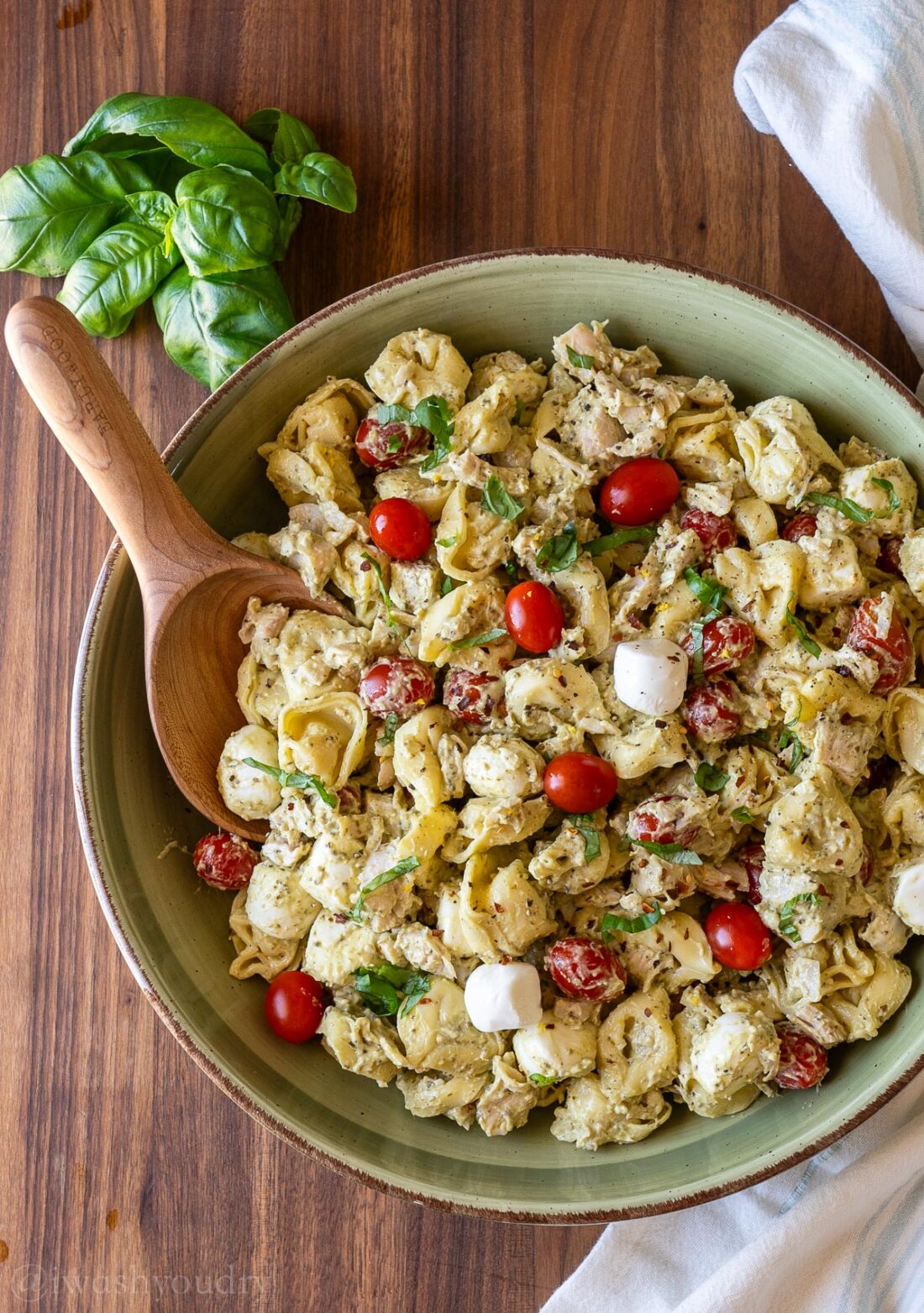 green bowl filled with tortellini pasta, tomatoes and chicken in a creamy pesto sauce.