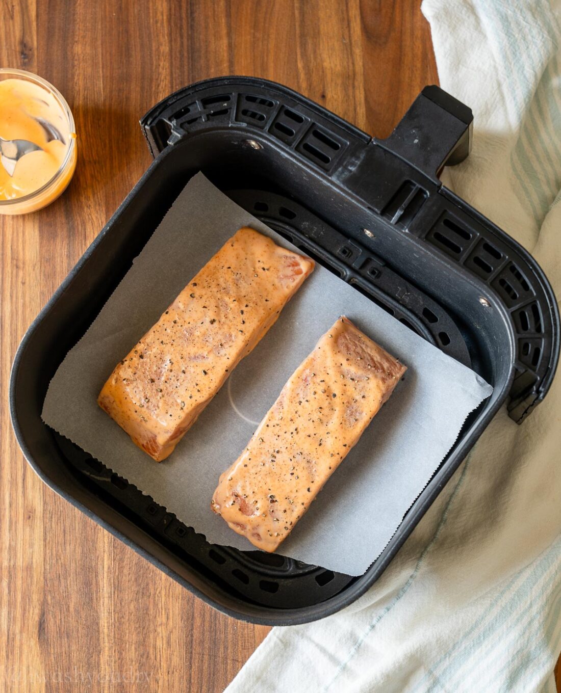 coated salmon in air fryer on top of parchment paper.