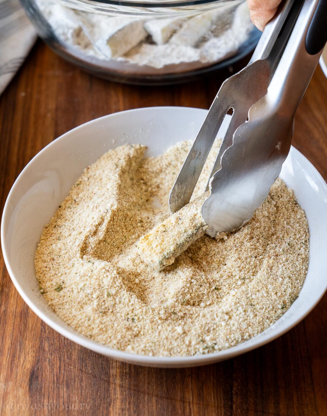 zucchini coated in breadcrumbs being held up with kitchen tongs.