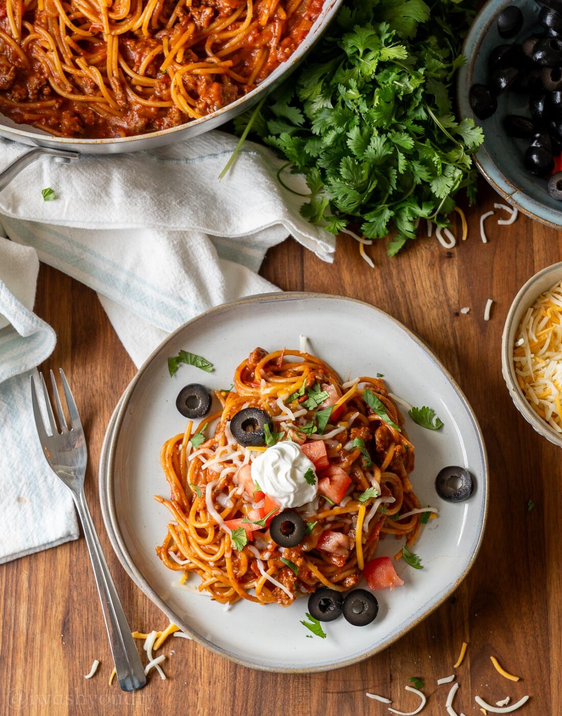 plate of taco spaghetti topped with sour cream, olives and tomatoes.