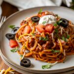 plate of spaghetti with taco meat and toppings.